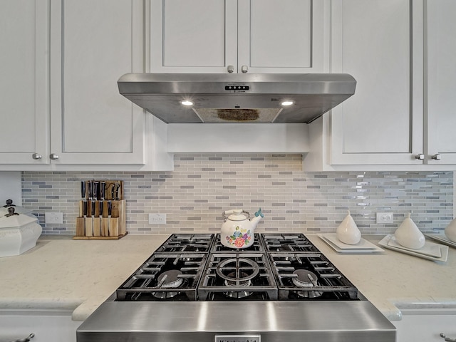 kitchen with under cabinet range hood, light stone counters, white cabinetry, decorative backsplash, and range