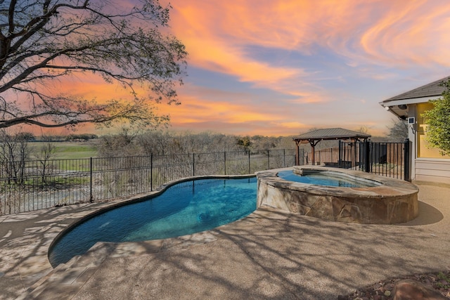 pool at dusk featuring a gazebo, a pool with connected hot tub, and fence