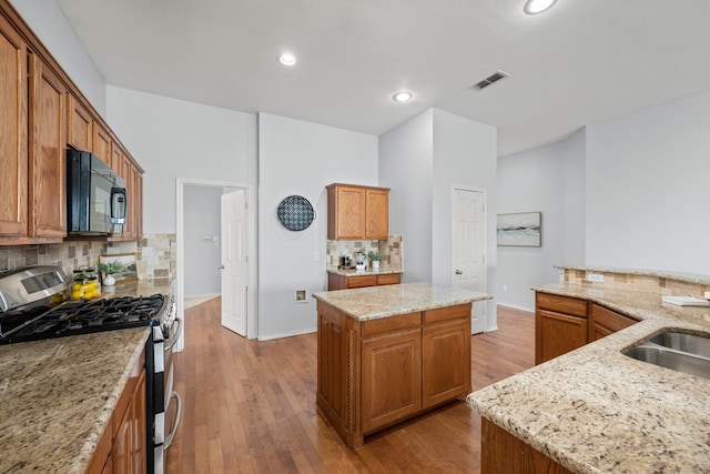 kitchen with visible vents, wood-type flooring, black microwave, gas range, and a center island