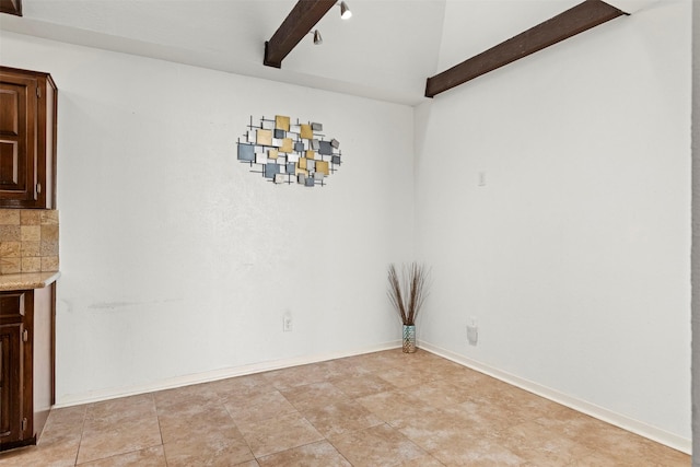 unfurnished dining area with beamed ceiling and baseboards