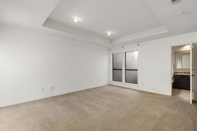 unfurnished bedroom featuring baseboards, a raised ceiling, light carpet, and connected bathroom