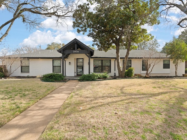 view of front facade with brick siding, a front yard, and a shingled roof