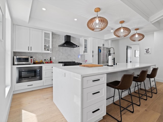 kitchen featuring backsplash, light wood-style floors, appliances with stainless steel finishes, and wall chimney exhaust hood