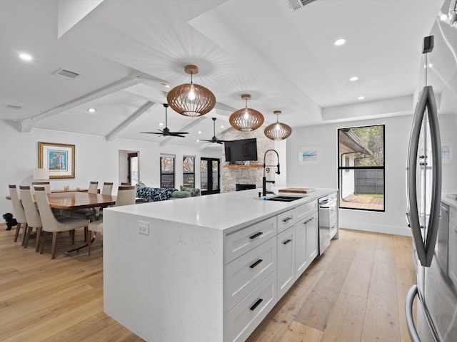 kitchen with visible vents, a stone fireplace, appliances with stainless steel finishes, light wood-style floors, and a sink