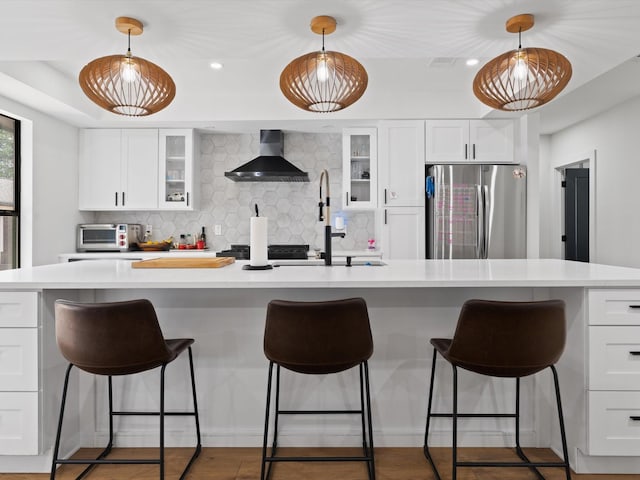 kitchen featuring wall chimney range hood, decorative backsplash, light countertops, and freestanding refrigerator