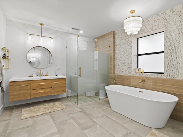 full bath featuring a notable chandelier, a stall shower, tile walls, a soaking tub, and vanity