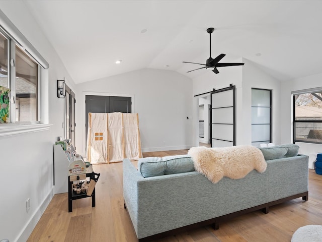 living area featuring a barn door, lofted ceiling, a ceiling fan, and light wood finished floors