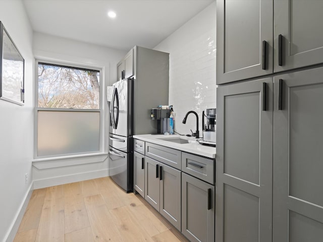 kitchen with gray cabinets, light wood-type flooring, stainless steel refrigerator with ice dispenser, and a sink