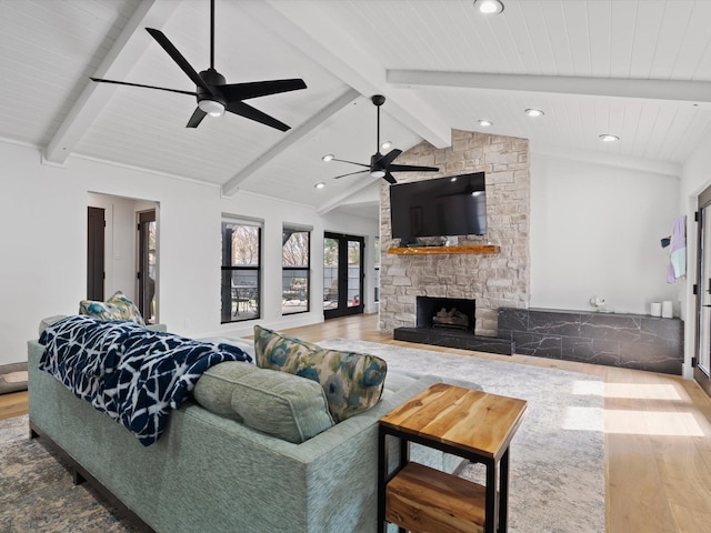 living room with a stone fireplace, lofted ceiling with beams, a ceiling fan, and wood finished floors