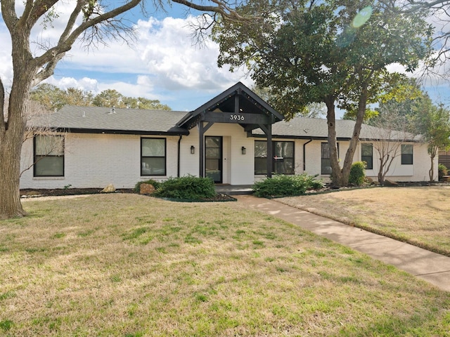 view of front of home with brick siding, a front lawn, and roof with shingles