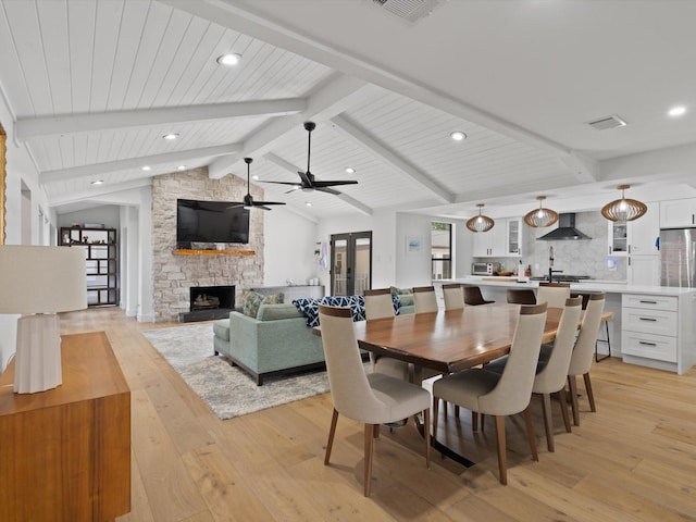 dining space featuring lofted ceiling with beams, plenty of natural light, a fireplace, and light wood finished floors