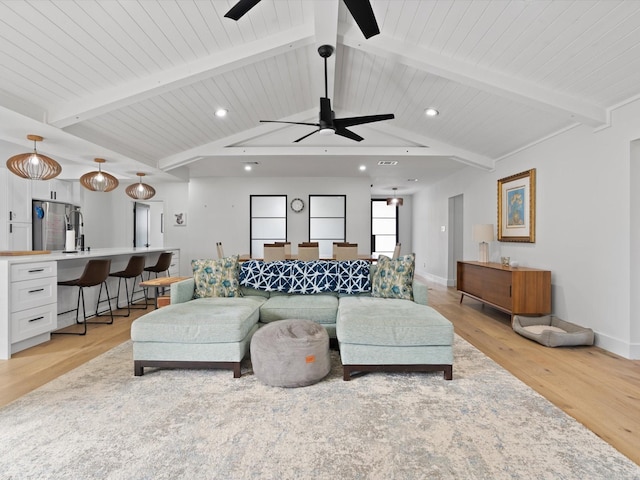 living room with lofted ceiling with beams, light wood-style flooring, a ceiling fan, and baseboards