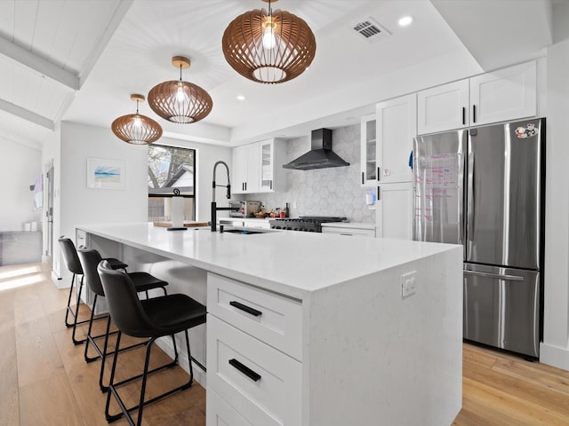 kitchen with visible vents, light wood-style flooring, tasteful backsplash, freestanding refrigerator, and wall chimney exhaust hood