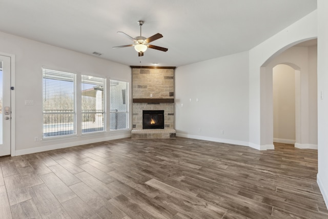 unfurnished living room with wood finished floors, baseboards, visible vents, arched walkways, and ceiling fan