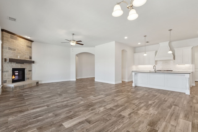 unfurnished living room with visible vents, baseboards, ceiling fan with notable chandelier, light wood-style flooring, and arched walkways