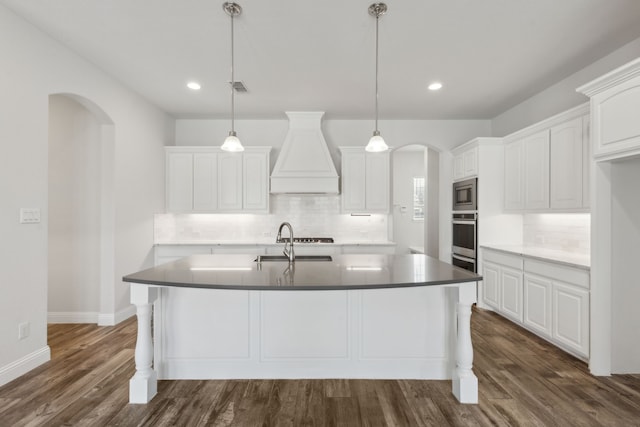 kitchen featuring stainless steel microwave, premium range hood, arched walkways, white cabinetry, and a sink