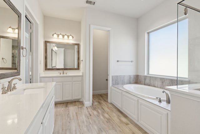 bathroom featuring visible vents, a garden tub, two vanities, wood finished floors, and a sink