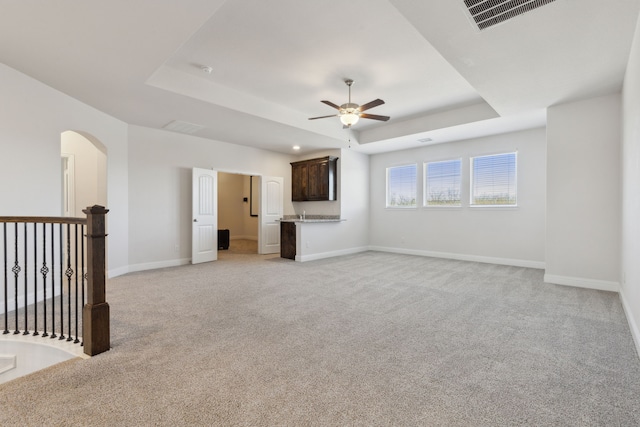 unfurnished living room with a tray ceiling, baseboards, visible vents, and ceiling fan