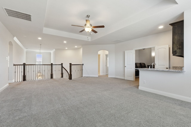 unfurnished room with visible vents, a ceiling fan, arched walkways, a raised ceiling, and light colored carpet