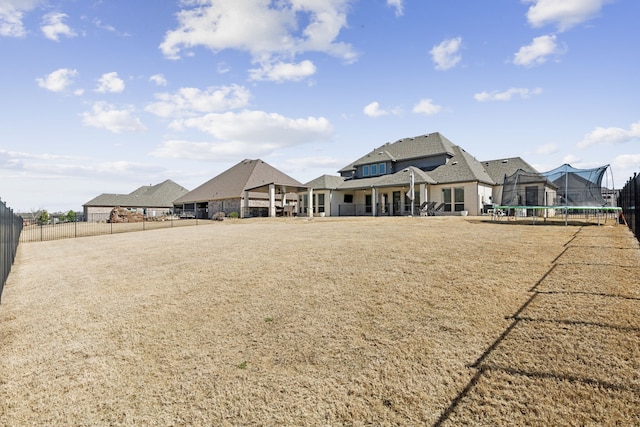 rear view of property featuring a patio, a trampoline, a lawn, and fence