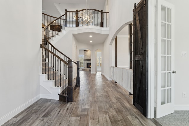 foyer entrance featuring wood finished floors, an inviting chandelier, arched walkways, a warm lit fireplace, and stairs