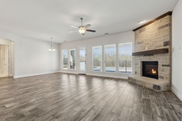 unfurnished living room featuring visible vents, ceiling fan with notable chandelier, wood finished floors, arched walkways, and a stone fireplace