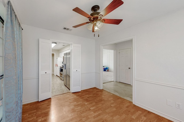 spare room featuring a ceiling fan, visible vents, light wood-style floors, and baseboards