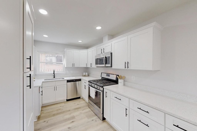 kitchen with light wood finished floors, recessed lighting, white cabinets, stainless steel appliances, and a sink