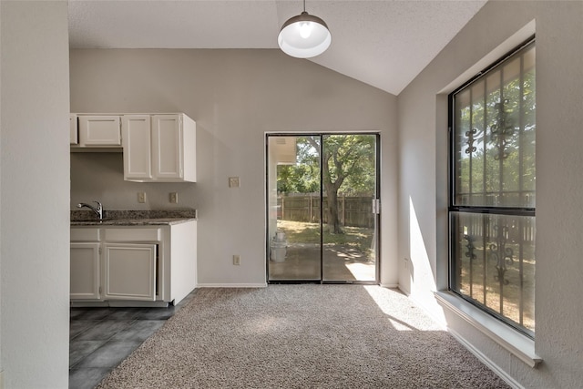 unfurnished dining area featuring lofted ceiling, a sink, dark carpet, and baseboards