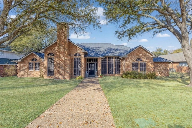 ranch-style home featuring brick siding, a chimney, a front lawn, and a shingled roof