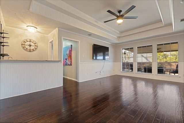 unfurnished living room featuring hardwood / wood-style floors, a ceiling fan, a wainscoted wall, a tray ceiling, and ornamental molding