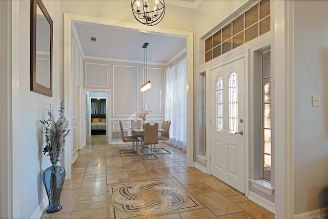 entryway with visible vents, stone tile flooring, an inviting chandelier, crown molding, and a decorative wall