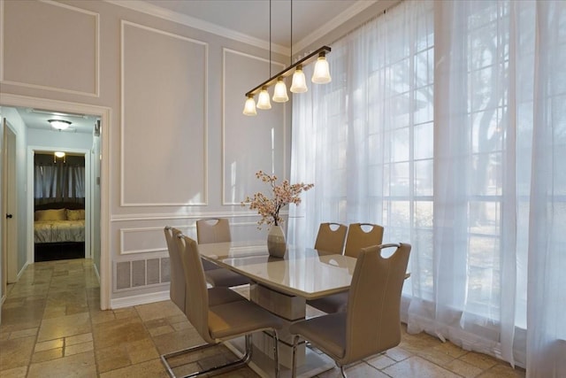 dining area featuring a healthy amount of sunlight, stone tile flooring, crown molding, and a decorative wall