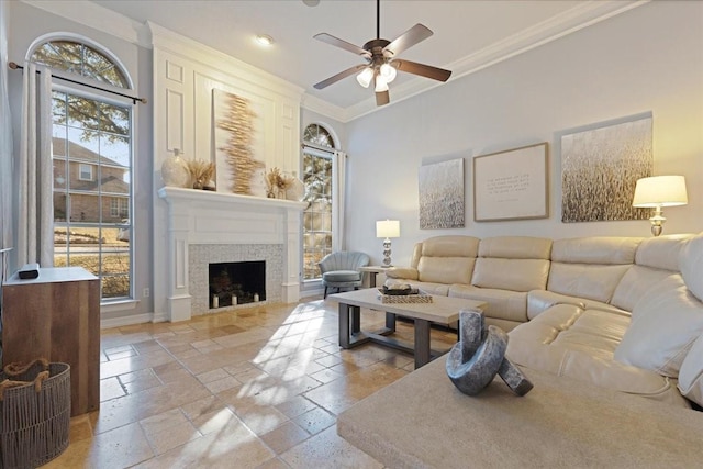 living room featuring baseboards, ceiling fan, ornamental molding, a fireplace, and stone tile flooring