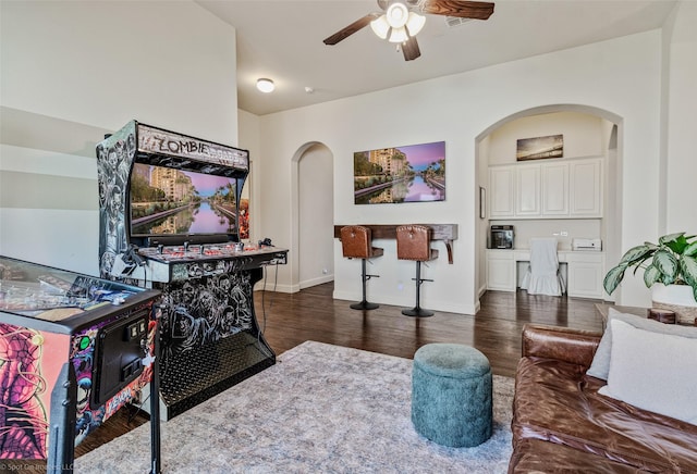 living area featuring baseboards, wood finished floors, arched walkways, and ceiling fan