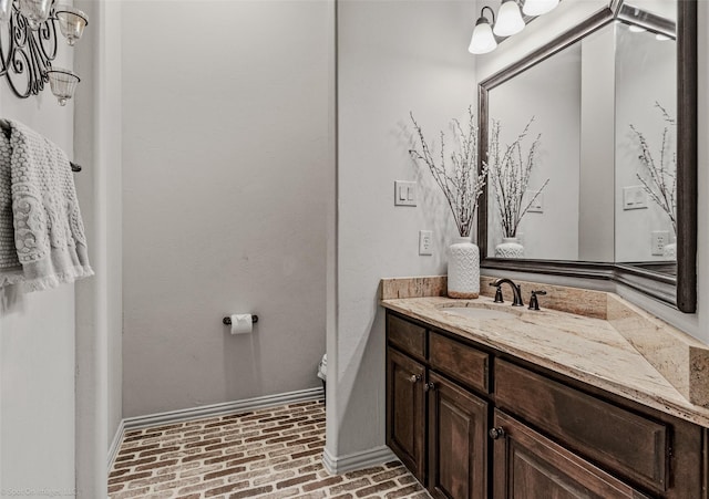 bathroom featuring brick floor, baseboards, toilet, and vanity