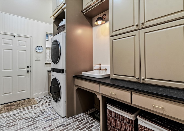 laundry room with stacked washer / dryer, cabinet space, brick floor, and a sink