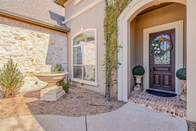 entrance to property featuring stucco siding, stone siding, and roof with shingles