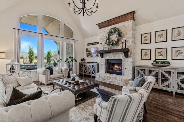 living room featuring a stone fireplace, high vaulted ceiling, wood finished floors, and a chandelier