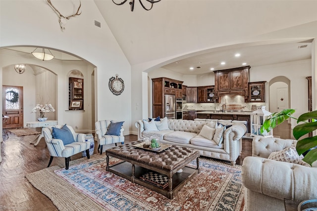 living room featuring visible vents, baseboards, wood finished floors, arched walkways, and high vaulted ceiling