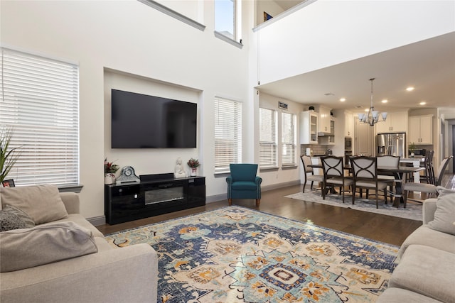 living area with baseboards, recessed lighting, an inviting chandelier, a towering ceiling, and dark wood-style floors