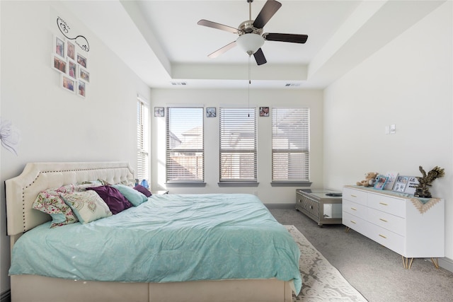 bedroom featuring visible vents, a tray ceiling, baseboards, light colored carpet, and ceiling fan