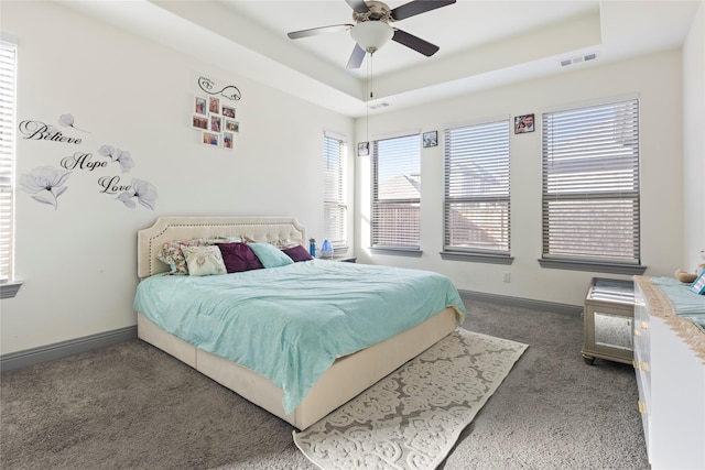 carpeted bedroom with a tray ceiling, baseboards, and visible vents