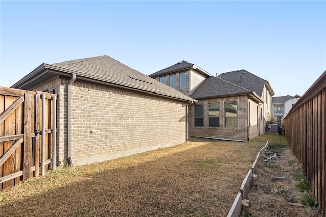 rear view of house featuring a yard, a fenced backyard, brick siding, and a shingled roof