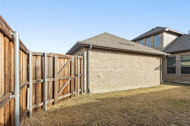 view of home's exterior with a gate, fence, roof with shingles, a yard, and brick siding