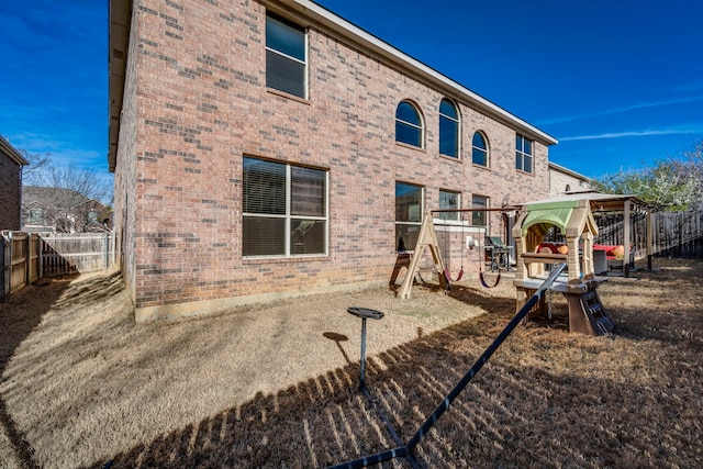 rear view of house with a playground, fence, and brick siding