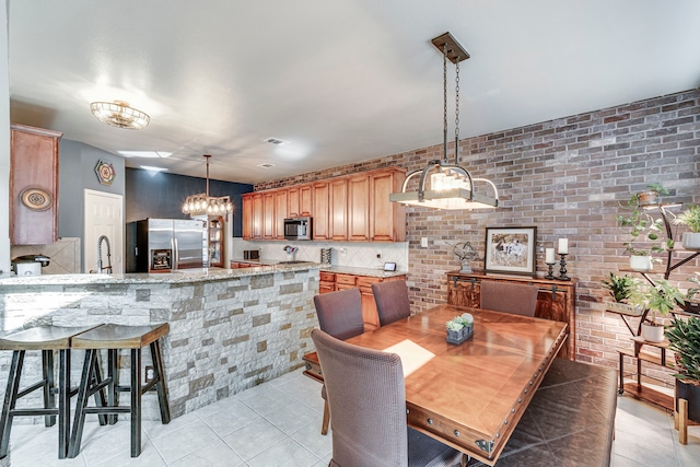 dining room featuring light tile patterned floors, a chandelier, and brick wall