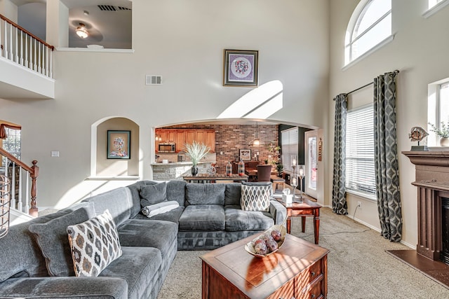 carpeted living room featuring stairway, visible vents, a towering ceiling, and a fireplace