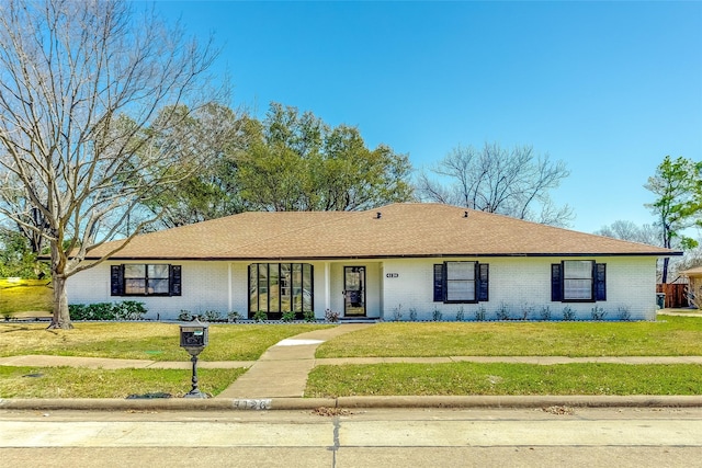 ranch-style home with brick siding, a front yard, and roof with shingles