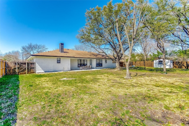 rear view of property featuring brick siding, an outdoor structure, a yard, a patio area, and a fenced backyard